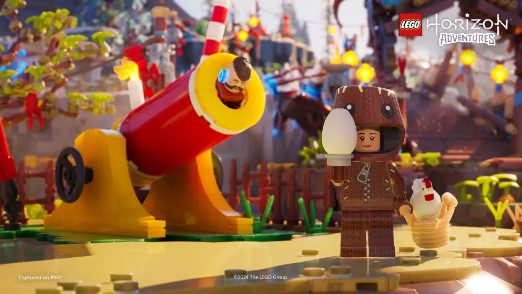 Um canhão de circo com um personagem Horizon rindo está logo atrás de outro personagem Horizon vestido de Sackboy em uma vila feita de LEGO.