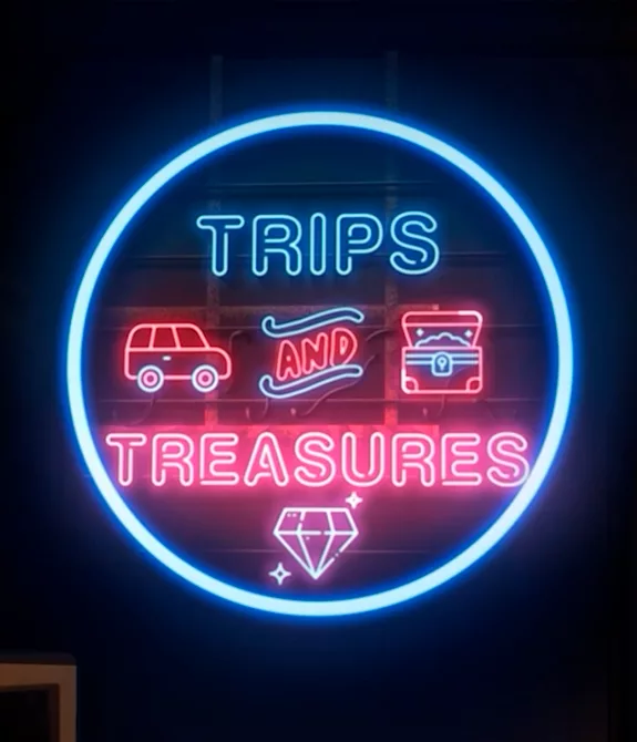 Pacific Drive Trips and Treasures com a imagem de uma garagem, um carro estacionado e um letreiro luminoso em azul e vermelho com o nome da atualização.